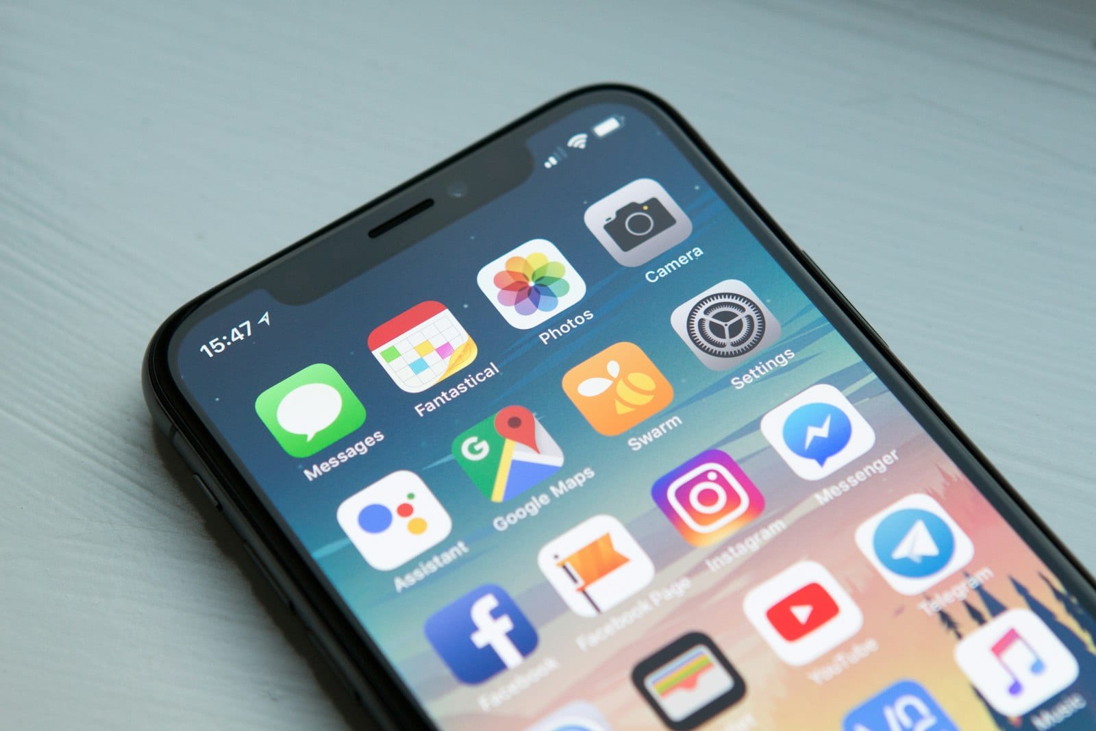 Hands holding a smartphone, thumbs mid-tap on a modern app interface, soft natural daylight on a desk