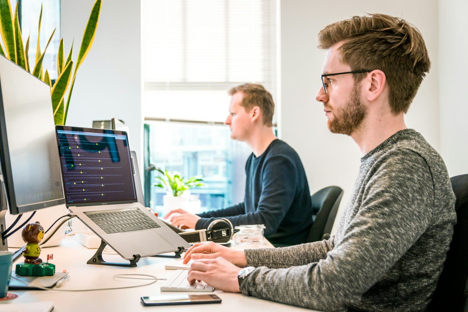 An engineer at a multi-monitor setup showing deployment pipelines and a metrics dashboard, whiteboard sketches softly blurred in the background